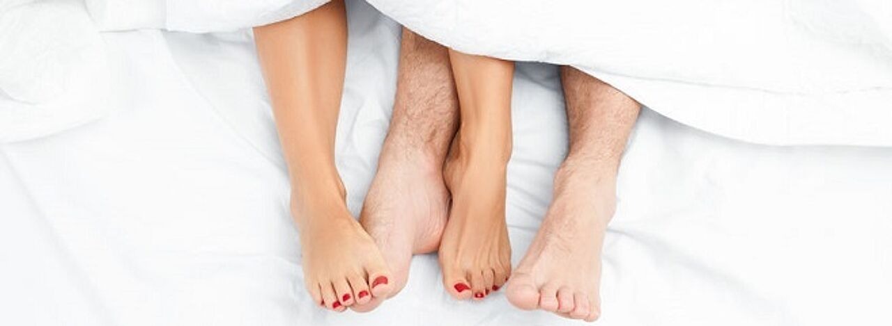 Füße von zwei Personen unter der Bettdecke