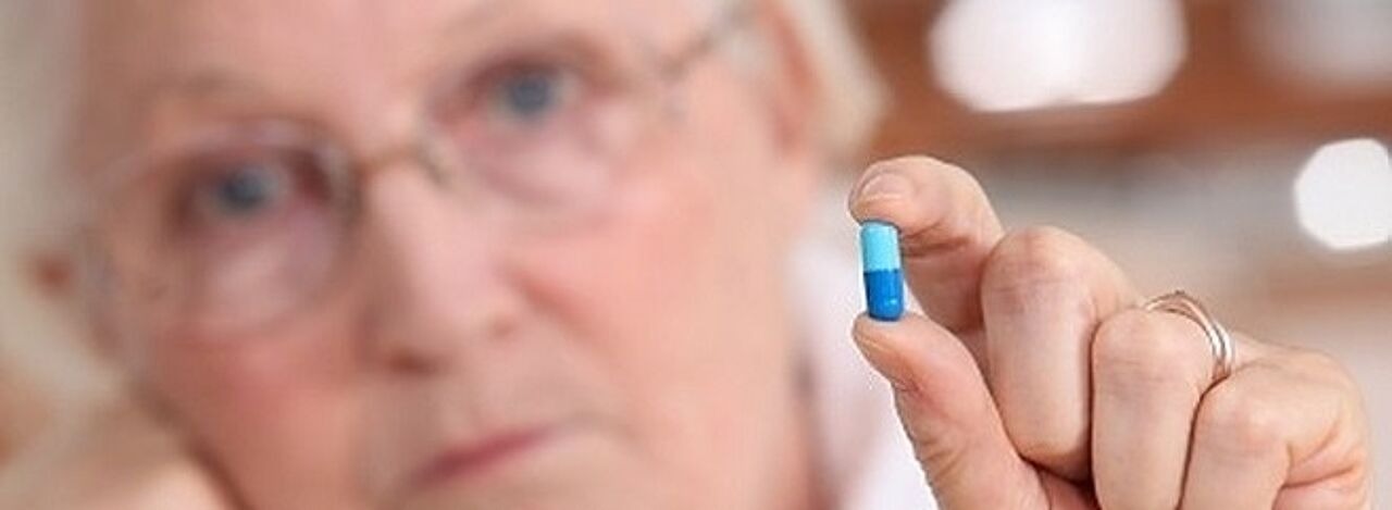 Ältere Frau hält Tablette zwischen den Fingern