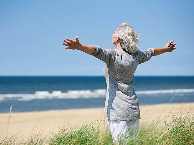 Tipps für Frauen zur Psychischen Gesundheit Ältere Frau steht mit ausgebreiteten Armen am Meer
