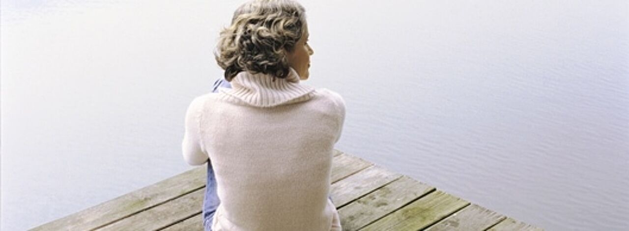 Frau sitzt am Steg und blickt auf einen See