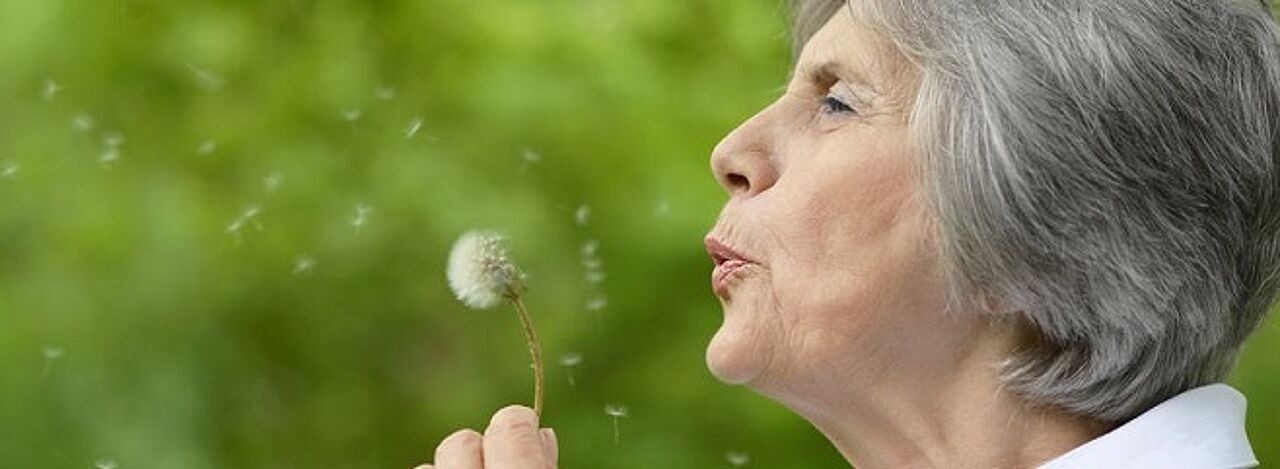 Ältere Frau pustet Pusteblume